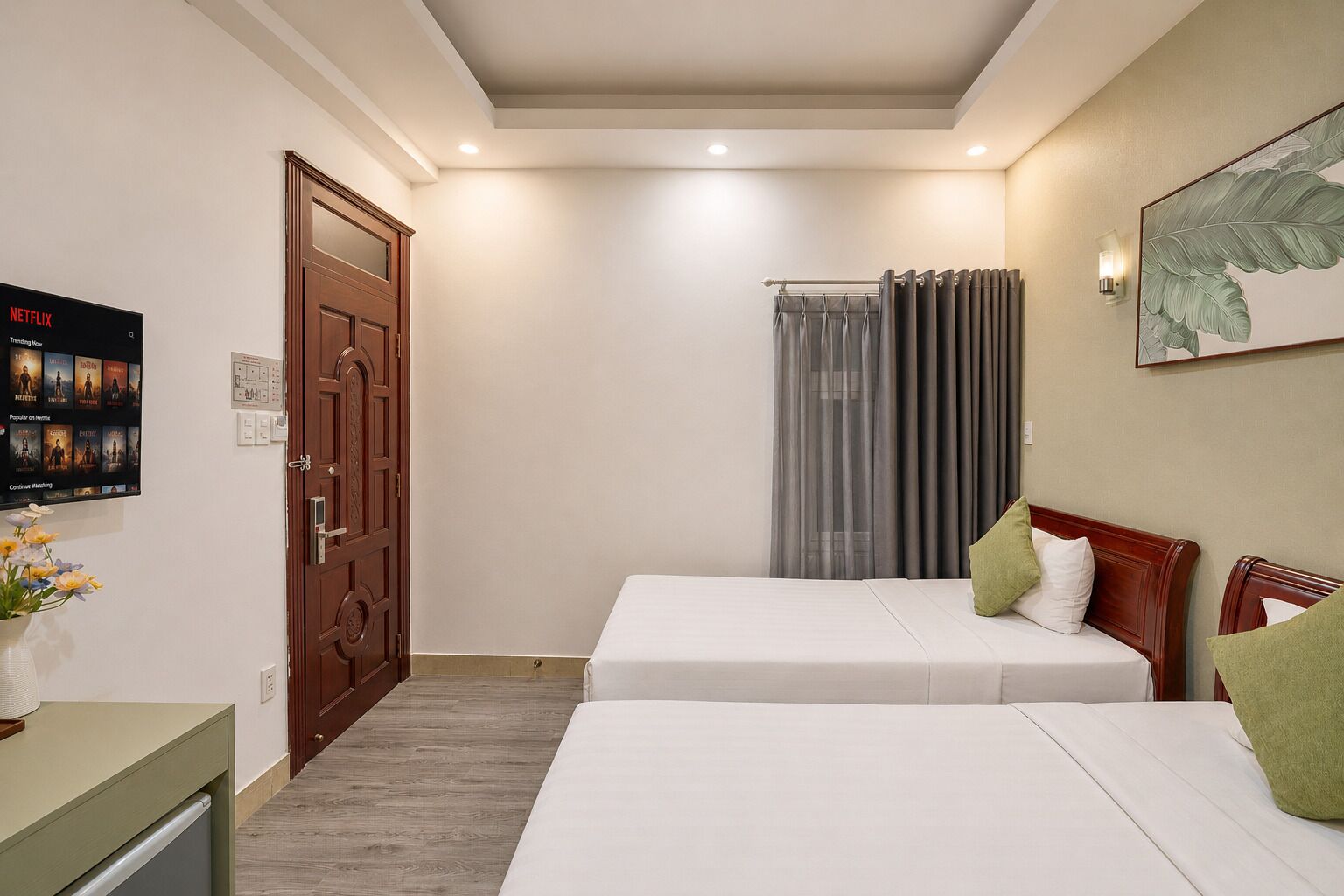Une chambre d’hôtel avec deux lits simples, une porte en bois, un petit bureau et un téléviseur fixé au mur diffusant du contenu Netflix.