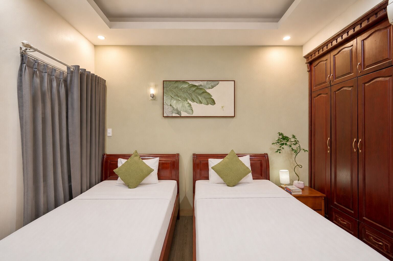 A hotel room with two beds, a large wooden wardrobe, a wall-mounted plant, and a framed artwork.