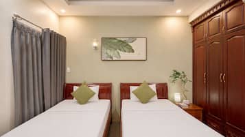 A hotel room with two beds, a large wooden wardrobe, a wall-mounted plant, and a framed artwork.