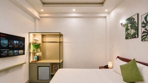 A hotel room with a bed, a desk with a lamp, a small fridge, a TV displaying Netflix content, and a wall with a plant. - Cactusland Hotel Tan Binh (Ho Chi Minh City)