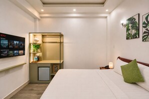 Ein Hotelzimmer mit einem Bett, einem Schreibtisch mit Lampe, einer kleinen Kühlbox, einem Fernseher, der Netflix-Inhalte zeigt, und einer Wand mit einer Pflanze.