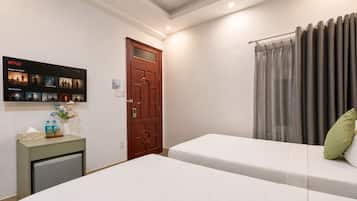 A hotel room with two beds, a wooden door, a wall-mounted TV displaying Netflix content, and a small table with a vase and bottles.