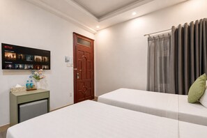 A hotel room with two beds, a wooden door, a wall-mounted TV displaying Netflix content, and a small table with a vase and bottles.