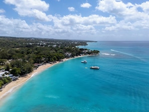Luftaufnahme einer Küstenlandschaft mit Strand, Booten und einem dicht bewaldeten Gebiet.
