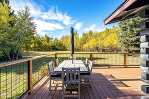A deck with a table and chairs, surrounded by a wooden fence and overlooking a grassy area with trees.
