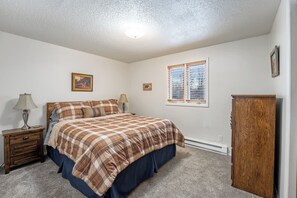 Une chambre à coucher comprenant un lit, des tables de chevet, une commode et une fenêtre avec des stores.