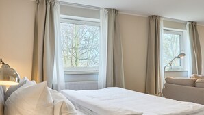 Habitación de hotel con cama, escritorio con lámpara y vista a árboles por la ventana.