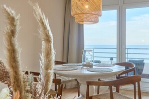 Ein runder Esstisch mit weißer Tischdecke, umringt von Holzsesseln. Auf dem Tisch steht ein Glas mit Sand und einer kleinen Pflanze.