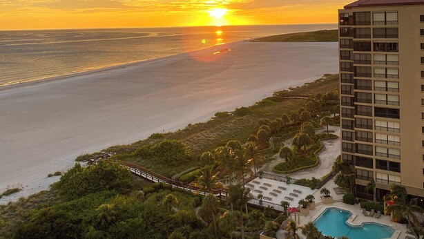 Ein Resort mit Schwimmbad, einer Brücke und Blick auf den Sonnenuntergang über dem Meer.