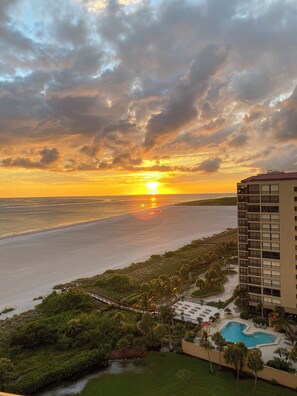 Un resort con piscina, un puente y vistas a la puesta de sol sobre el océano.