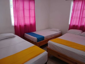 Ein Zimmer mit drei Einzelbetten, jedes mit einer anderen farbigen Bettdecke (gelb, blau und weiß).