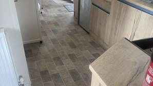 A kitchen with a tiled floor, a refrigerator, a dishwasher, and wooden cabinets.