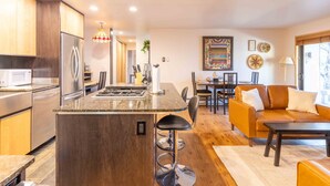 A modern kitchen with a central island, stainless steel appliances, and a dining area with a sofa and table. - Elkhorn Retreat: Condo with Pond Views, Pool & Pet-Friendly (Sun Valley)