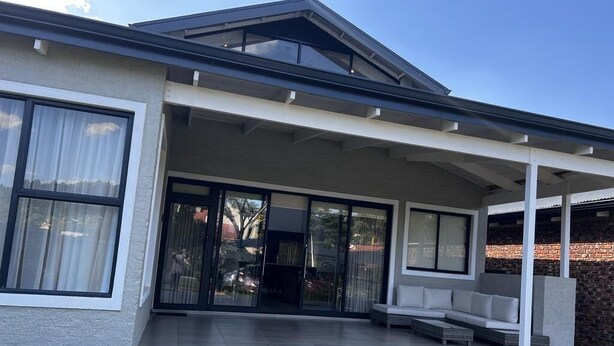 Et moderne hus med en overdækket terrasse, store skydedøre og en murstensvæg.