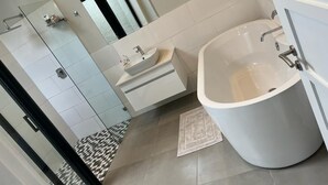 Et moderne badeværelse med et stort badekar, et separat bruseområde og en vaskebord med håndvask.
