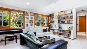Una sala de estar moderna con un sofá de cuero negro, un piano y una estantería llena de libros.