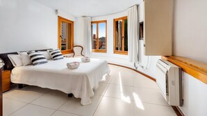Habitación de hotel con cama, una silla, un televisor y ventana con vista a la ciudad.