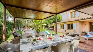 Un espacio de comedor al aire libre cubierto, con techo de madera, vajilla blanca y sillas color beige.