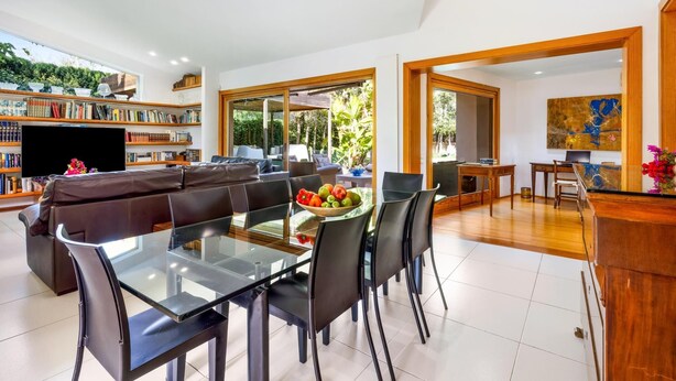 Una sala de estar moderna con una mesa de comedor de vidrio, un sofá de cuero y una estantería llena de libros.