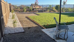 Ein Garten mit einer Terrassenfläche, einem Kiesweg und einem Rasen.