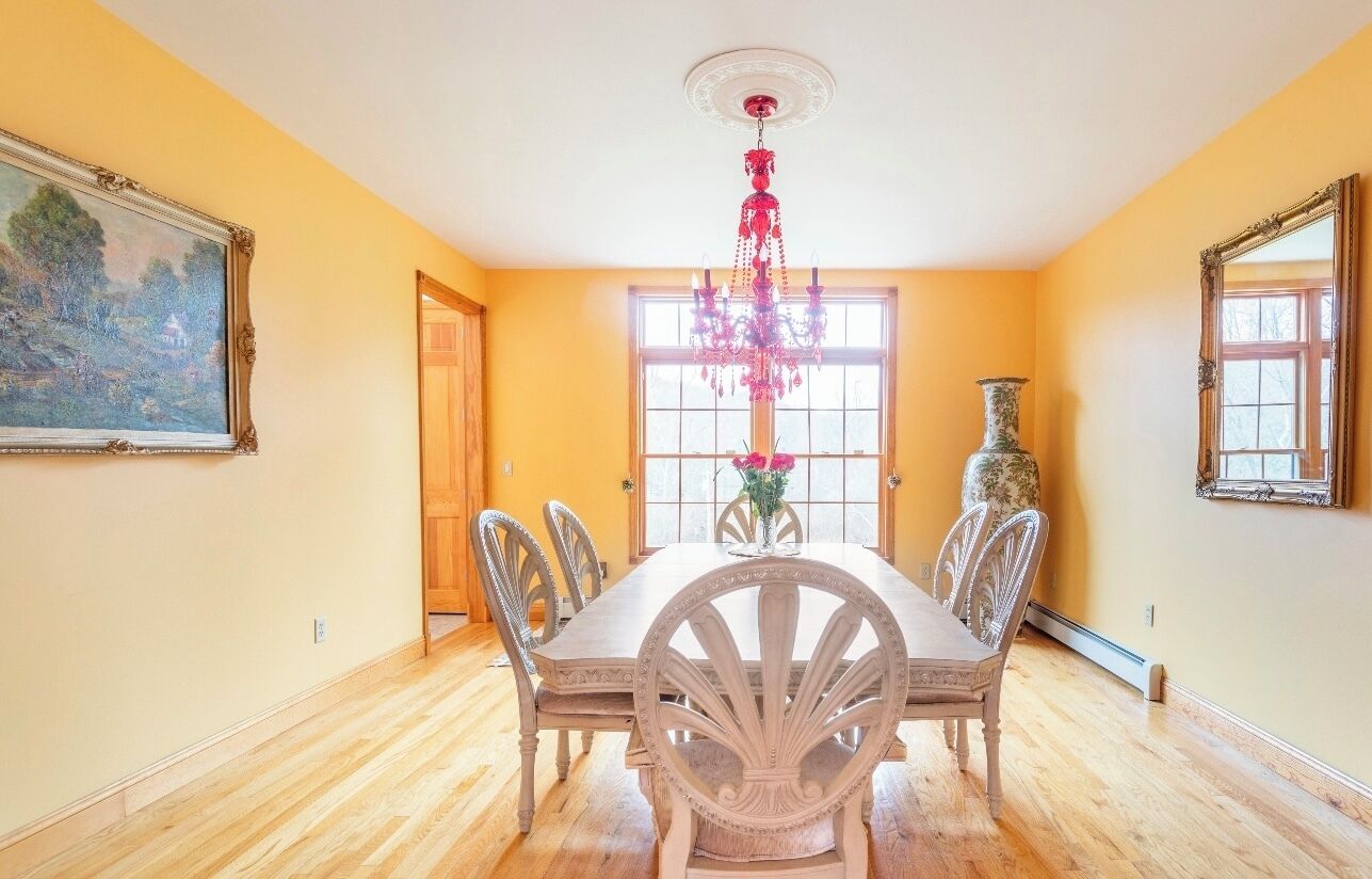 A dining room with a wooden table and chairs, a chandelier, and a vase with flowers.