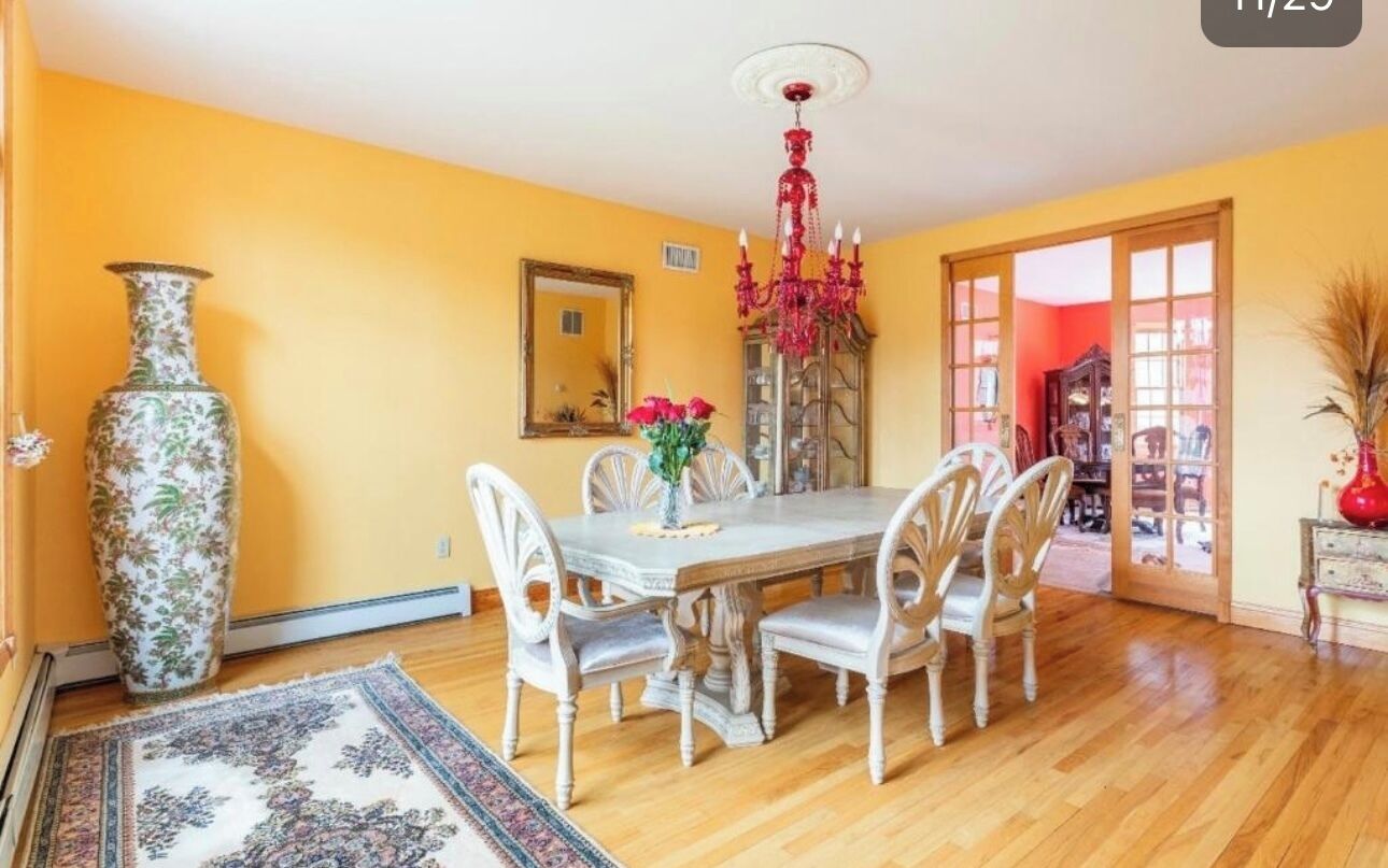 A dining area with a wooden table, white chairs, a large vase, and a chandelier.