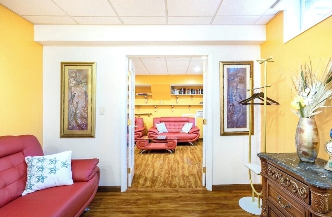 A room with a red sofa, a wooden floor, and a bookshelf in the background.