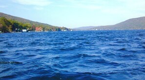 Vista de un lago con una orilla lejana, casas y colinas.