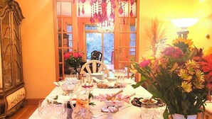 Una mesa de comedor con cristalería, un cuenco de manzanas, un calabaza y un jarrón de flores.