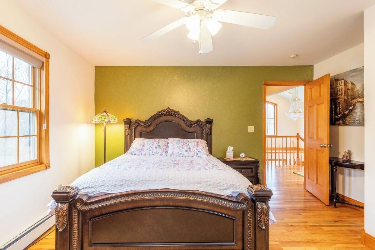 A bedroom with a wooden bed, a ceiling fan, a nightstand, a lamp, and a view of a balcony.