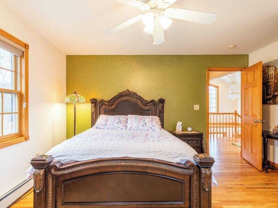 Ein Schlafzimmer mit einem hölzernen Bett, einem Deckenventilator, einem Nachttisch, einer Lampe und Blick auf einen Balkon.