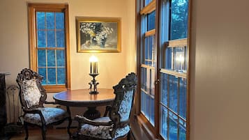A dining area with a table, two chairs, a rug, and large windows with a view of trees.