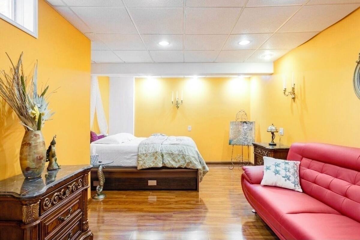 A bedroom with a bed, a red sofa, and a nightstand with a lamp.