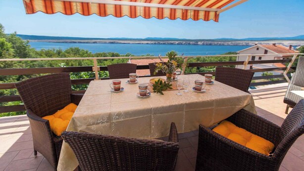 Una terrazza con mobili in vimini, un tavolo apparecchiato per mangiare e vista sul mare.