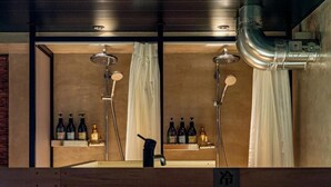 Un bagno moderno con due soffioni doccia, una panca in legno e uno scaffale con flaconi.