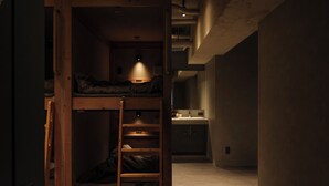 Una stanza piccola e poco illuminata, con un letto a castello, una scrivania e una singola lampada.