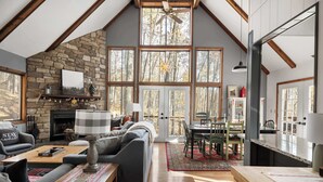 A cozy living room with a stone fireplace, a sofa, a coffee table, and a dining area with a red rug.