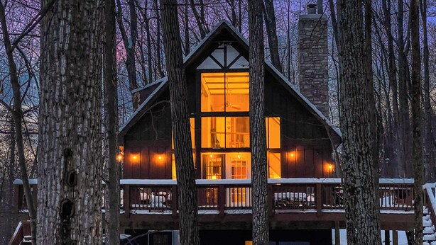 A log cabin with a central chimney, multiple windows, and a balcony.