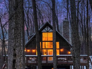 Une cabane en rondins avec une cheminée centrale, de nombreuses fenêtres et un balcon.