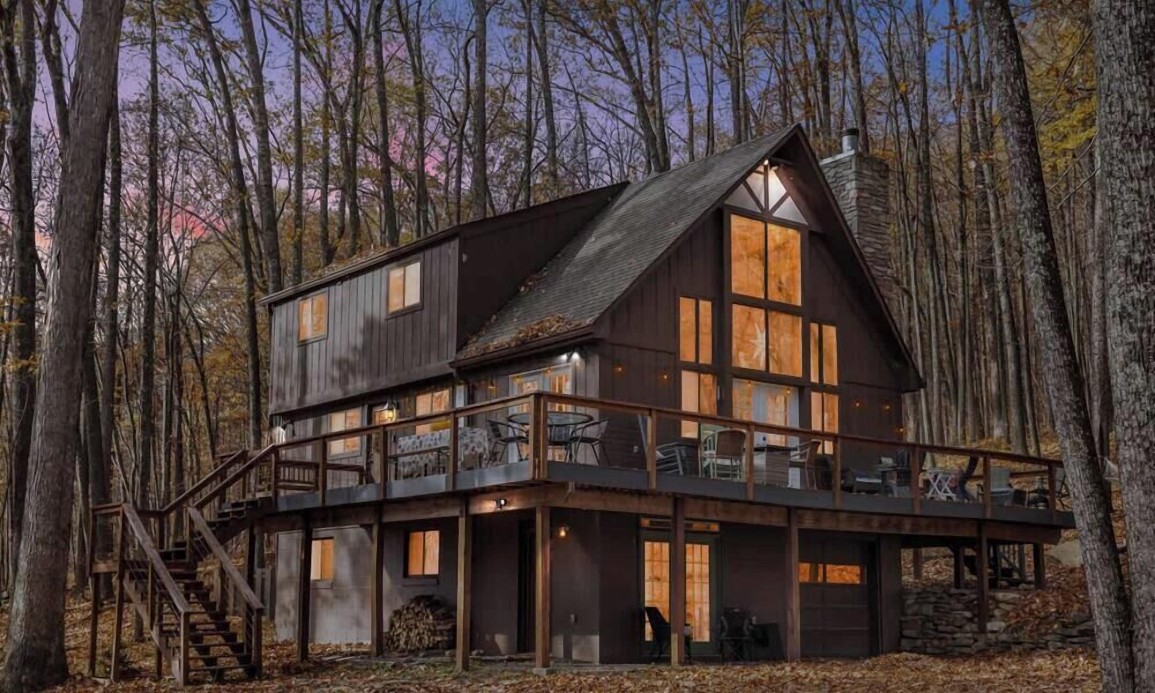 A two-story cabin with a balcony, surrounded by trees.