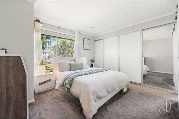 A bedroom with a bed, a window, a wardrobe, and a mirror.