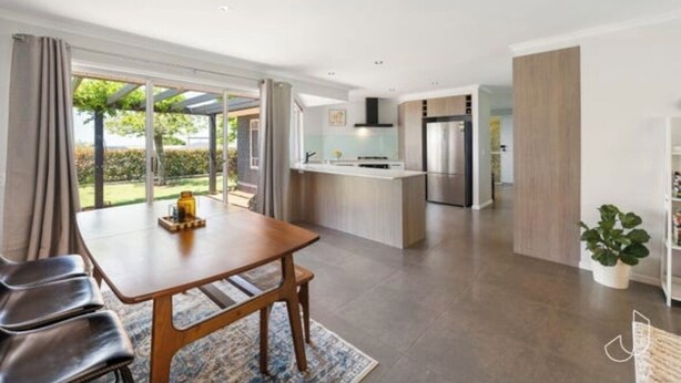 Una cocina moderna con una isla central, un comedor con mesa y sillas de madera, y vistas a un jardín a través de amplios ventanales correderas.