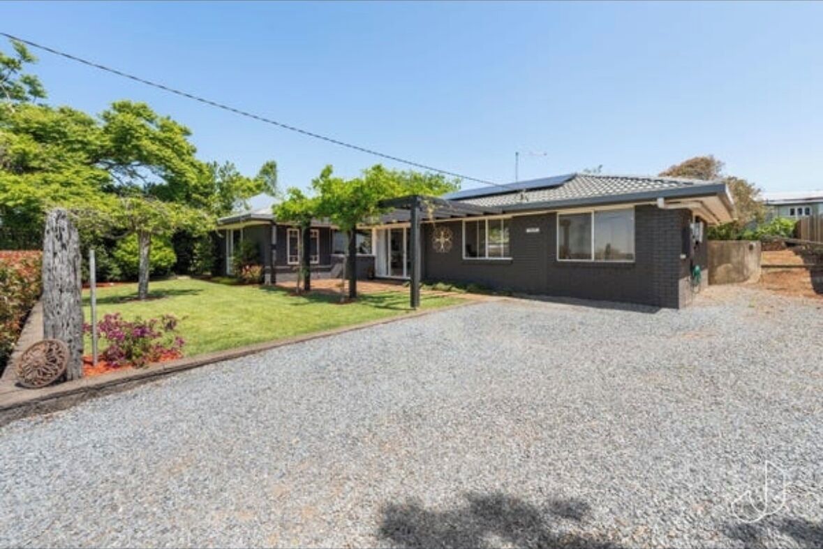 Una propiedad residencial con entrada pavimentada, césped y una casa de exterior oscuro.