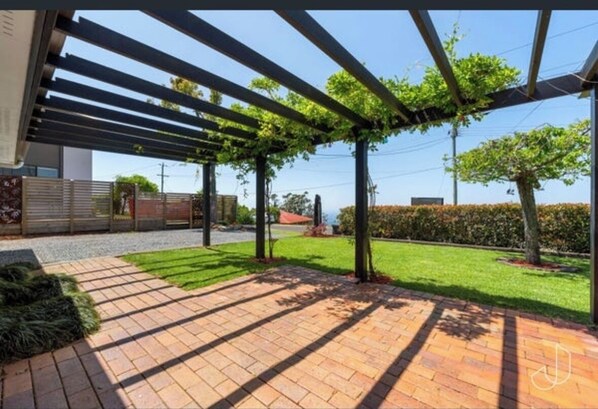 A covered outdoor area with a brick pathway, green lawn, and trees.
