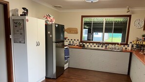 Uma cozinha com geladeira, pia e janela com vista para o verde.