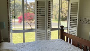 Quarto com cama, ventilador de teto e vista para um jardim através de venezianas abertas.