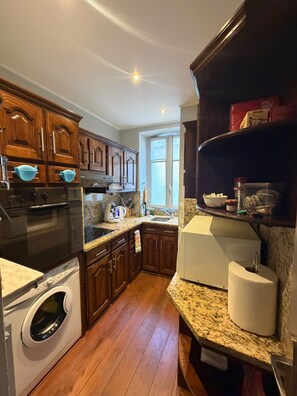 A kitchen with wooden cabinets, a built-in oven, a washing machine, granite countertops, and a window providing natural light.