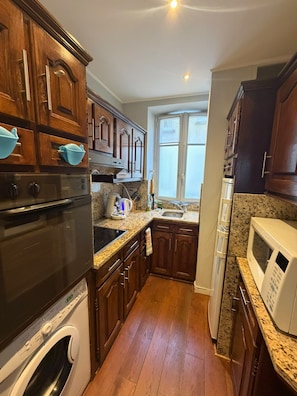 Una cocina con armarios de madera, horno de acero inoxidable, microondas y lavadora integrada.
