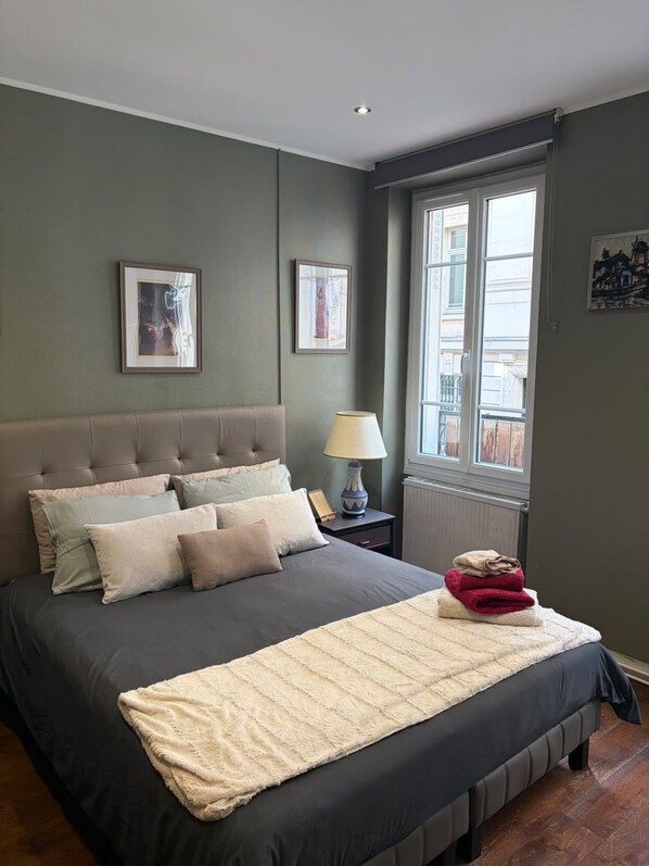 A bedroom with a large bed, a nightstand, a window, and two framed pictures on the wall.