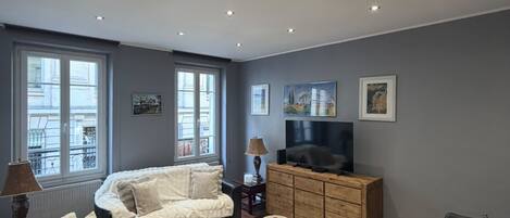 A modern living room with a sofa, a coffee table, a TV, and a dining area with chairs and a table.